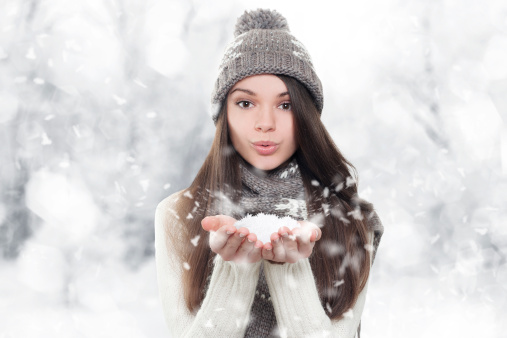 Winter portrait. Young, beautiful woman blowing snow toward camera on winter background