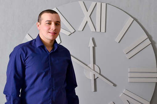 Man smiling against white clock. Young man smiling, positive, relaxed, satisfied attitude, against white clock. Business concept. Free space. High quality photo.