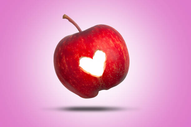 Vibrant red apple resting on a wooden table, illuminated by a warm beam of sunlight, creates a striking contrast against the surrounding dark background, enhancing its fresh, juicy appeal