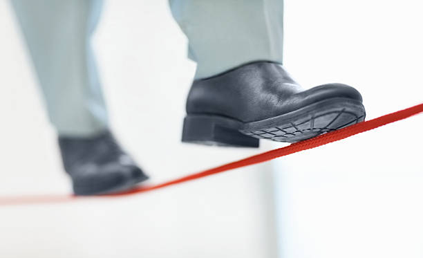 Business man walking on thin line depicting uncertainty job Unstable job - Low section of a business person walking on thin red line tightrope stock pictures, royalty-free photos & images