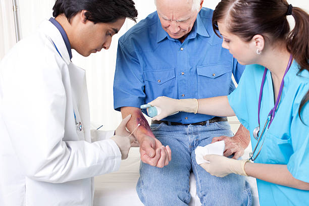 Doctor, nurse treating man's wound, burn.  Emergency room hospital. Series:  doctor, nurse and patient all looking at burn wound.  Mixed races.  Middle Eastern and Caucasian.  Emergency, urgent care treatment.  Hospital. wounded stock pictures, royalty-free photos & images