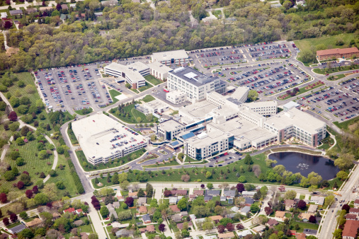 Aerial view of a large hospital facility showing the main entrance, heliport, multiple parking lots a water fountain and bordered with homes. Shot from the open window of a small airplane.\u2028http://www.banksphotos.com/LightboxBanners/Aerial.jpg