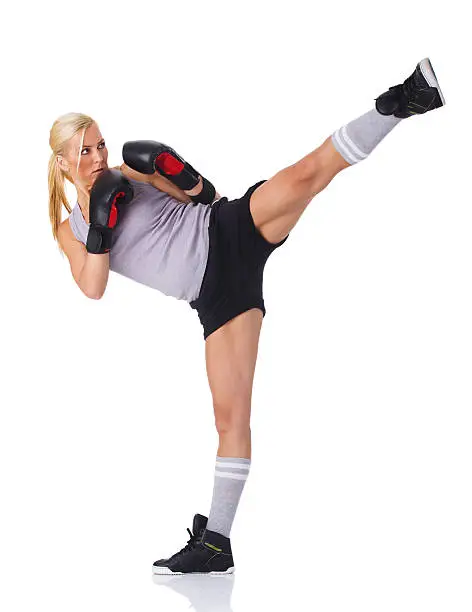 An athletic woman wearing gray work out clothes and boxing gloves,  kicking high sideways,  isolated on white