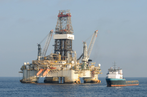 A floating deep water  semi-submersible oil drilling platform on location at sea with a supply vessel near.