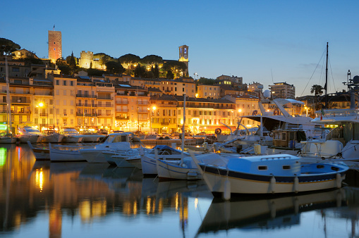 Panorama of Cannes, at dusk. French Riviera. Some motion blur on the water and boats due to long exposure. HDR. Sailing and motorboats moored in the harbor, Lights from the illuminated houses reflect beautifully in the water. Viewed from the harbor at night. Mediterranean Sea, French Riviera. 