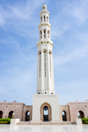 Translation of the Arabic Text (In The name of Allah the most gracious the most merciful) on a high minaret of a mosque with a green dome, with a cloudy blue sky at the day light, a beautiful mosque, selective focus