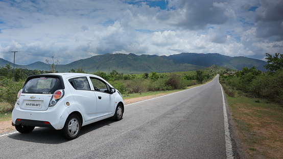 Mysuru, Karnataka, India-May 3 2023; A Dramatic picture of a white Car on a country road in the picturesque locale of a Mountain range near Mysore in Karnataka, India.
