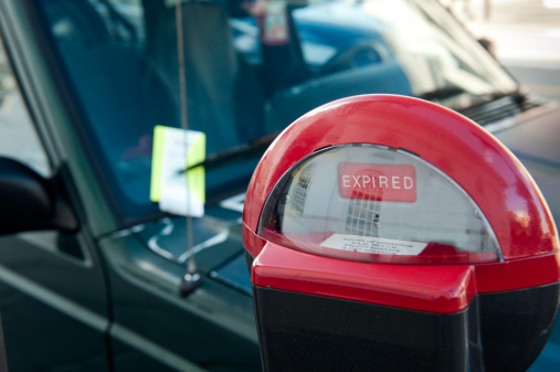 A car parked next to an expired parking meter has been adorned with a parking ticket under the wiper blade.