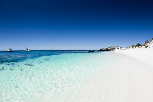 beautiful white sand and turquoise blue water with sailing ships under clear summer sky. the perfect beach. Rottnest Island, Western Australia. 