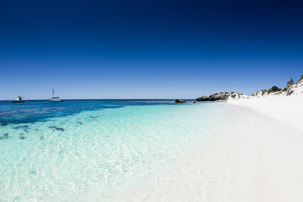 Beach with white sand and clear blue water and sky beautiful white sand and turquoise blue water with sailing ships under clear summer sky. the perfect beach. Rottnest Island, Western Australia.  rottnest island photos stock pictures, royalty-free photos & images