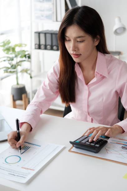 istock Young Asian businesswoman working on her project while using calculator in the office room. 1576057997