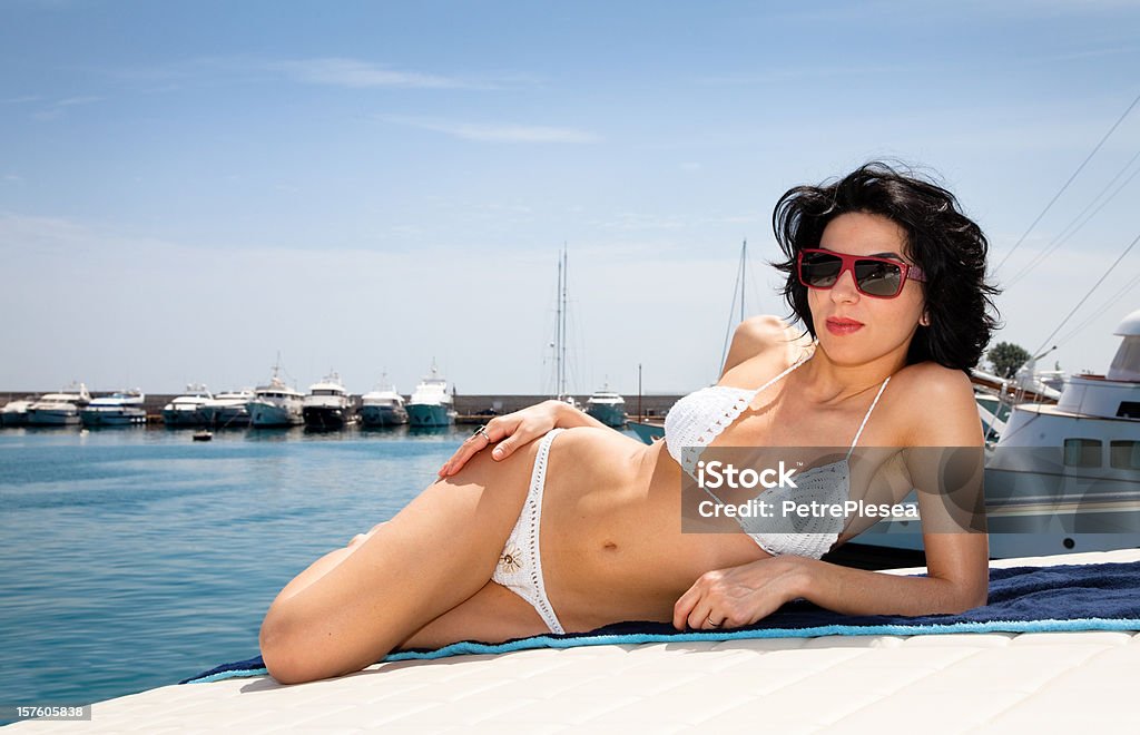 Belle jeune femme prenant un bain de soleil sur un yacht de luxe dans le port - Photo de 20-24 ans libre de droits