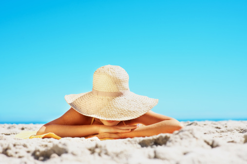 Woman lying on sandy beach in a big sun hat with copy space against clear blue sky