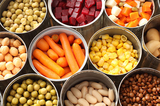 High angle view of cans filled with vegetables Twelve cans of open vegetables sit next to one another in three rows. There are peas, carrots, beats, snow peas, corn, chick peas and Lima beans in the cans. canned food stock pictures, royalty-free photos & images