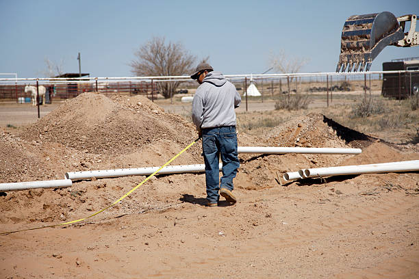 Construction site with workers laying pipes and cables, using machinery and tools