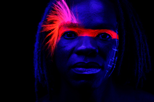 Portrait of a man under black lights with glowing hair, and makeup.  No filters were used to create this effect - this is UV lighting creating the glow-in-the-dark hair, and makeup.  Extremely low light situation with high ISO settings.
