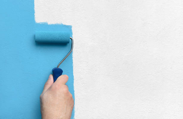 istock Blue color painting wall with roller in hand 1576070173