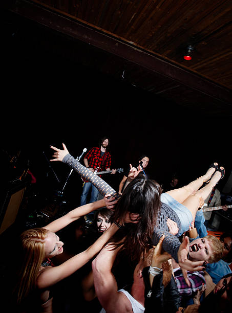 Crowd Surfing at a Rock Concert Young woman crowd surfing in the mosh pit with band in the background. mosh pit stock pictures, royalty-free photos & images