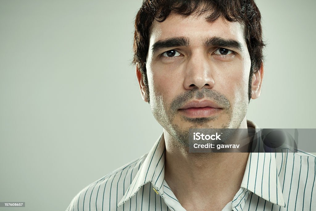 confident man with strong, angular masculine face looking at camera Indoor, studio portrait of a confident, fashionable and elegant man against a plain background with angular masculine face wearing a striped shirt and looking at the camera. Men Stock Photo