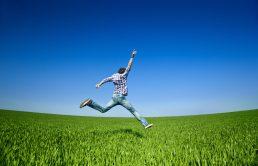 Young man jumping over green field.