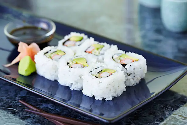 California roll on blue rectangular plate with wasabi, ginger and soy sauce.  Shot with shallow focus on front sushi.