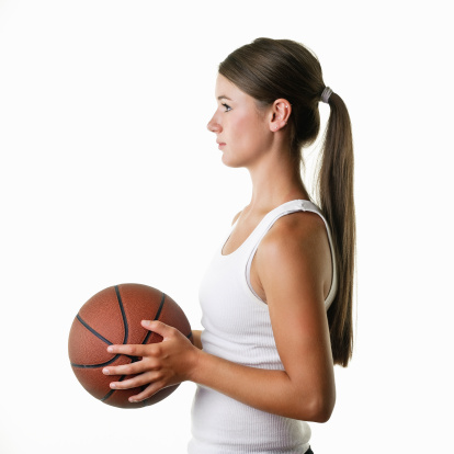 Young woman in sports clothing and holding basketball against white background, side view.