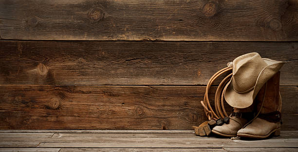 Western barnwood background w/boots,hat,lasso-extra wide Cowboy hat,boots,lasso,spurs and riding gloves on the right side of a plain,weathered,rustic barnwood background.  room for title and/or text. Extra wide and large file size for a banner format.http://www.garyalvis.com/images/wildWest.jpg boot photos stock pictures, royalty-free photos & images