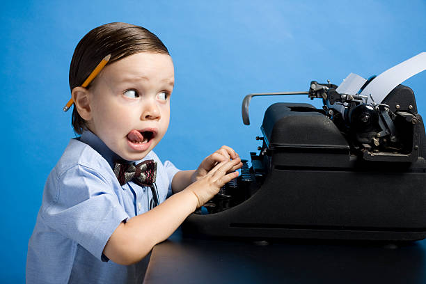 Young boy with bow tie and pencil using typewriter stock photo