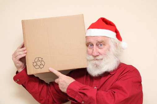 portrait of a kindly man with a white beard in a santa hat - carrying a large cardboard box, happy to be recycling 
