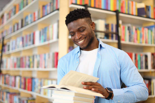 istock Black smiling student in book store holding a book and looking at it 1576110410
