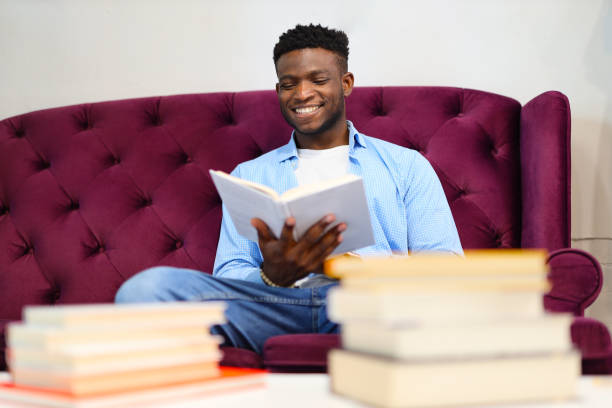 istock Positive black student on the couch reading a book in the library. 1576110422