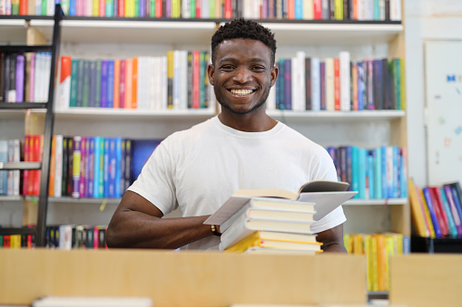 Smiling black guy with books in the library.