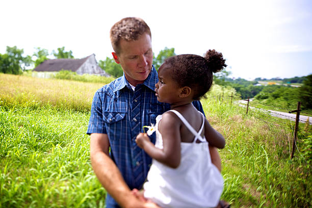 Father playfully lifting his smiling daughter while enjoying a sunny day in the countryside