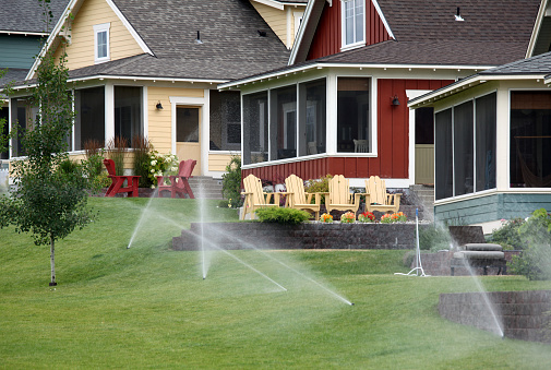 Water sprinklers irrigating a beautifully landscaped neighbourhood. Irrigation and water conservation are critical issues for urban environments. Water usage and water shortages are more and more common. This is a residential irrigation system that is irrigating beautiful lawns in summer. 