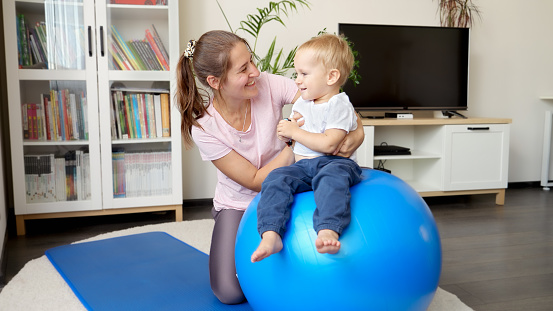 Little baby boy with young mother doing fitness on fitball in living room. Concept of healthcare, sports, yoga and kids development.