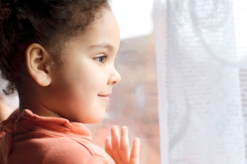 Royalty free stock photo of happy 3  years old girl looking through window. 