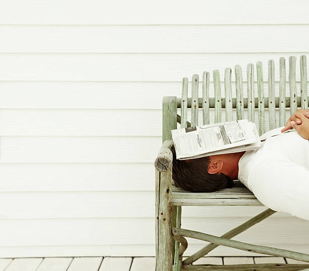 istock Man fast asleep on wooden bench with newspaper over face 157612560