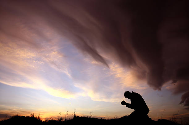 Silhouette of Unrecognizable Caucasian Man Praying During Storm stock photo