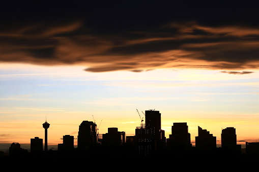 Calgary, Alberta, Canada with dramatic Chinook cloud. Silhoutte with sunset sky. The Calgary Tower and a number of construction cranes highlight the scene. Calgary, Alberta is a prominent oil and gas city with many oil and gas companies occupying downtown real estate. This image is taken near the Calgary zoo and is looking west towards the Rocky Mountains. Nobody is in the image. 