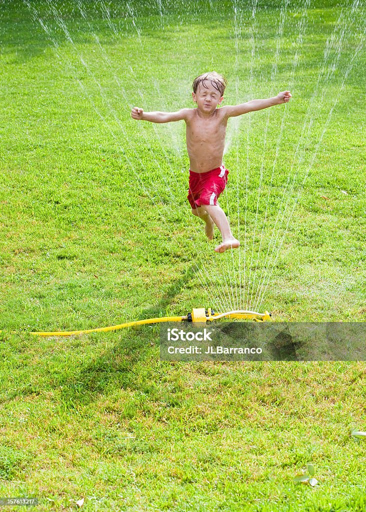Ragazzino i salti in uno Sprinkler - Foto stock royalty-free di Annaffiatore
