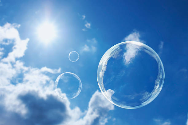 Floating Soap Bubbles Against Clear Sunlit Blue Sky and Clouds stock photo