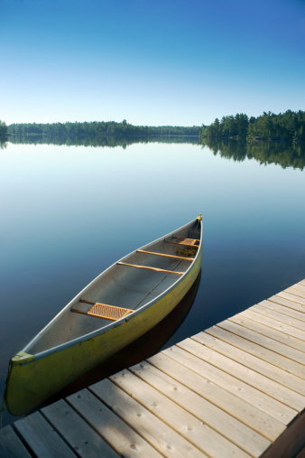 An aluminum canoe tied to a lakeside dock in the Kawartha region of Ontario, Canada. This is a typical early morning scene for thousands of Canadians on Summer vacation.