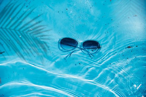 Sun glasses under water in the blue sea in palm leaf shade. Abstract Summer party background. Copy space for advertising