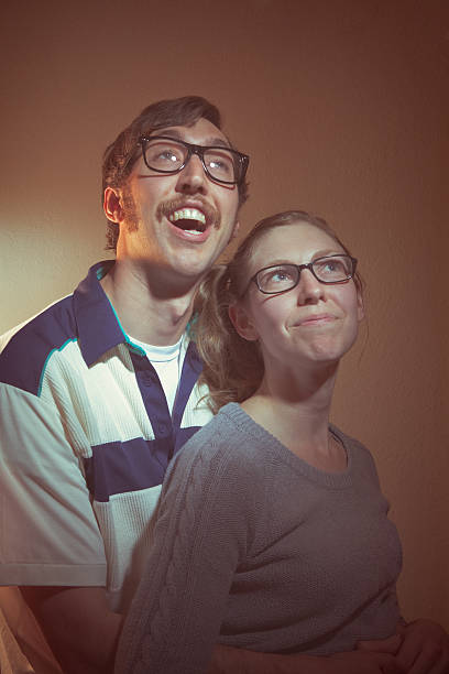A nerd couple from the 1960s or 1970s poses for a family picture.  Intentional low contrast and washed out brown effect for aged feel and style.  Vertical.