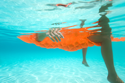 underwater shot of woman on vacation floating on orange raft in the Caribbean water