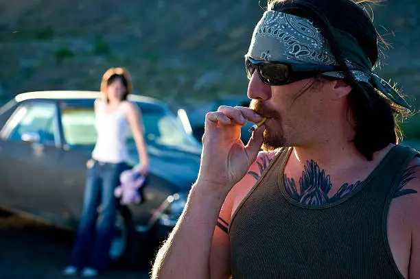 Photo of Rustic man smokes in front of girlfriend and el camino