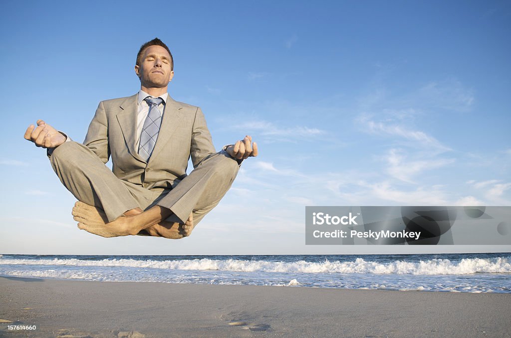 Peaceful Meditating Businessman Levitating Above Tranquil Beach Businessman closes his eyes and levitates with crossed legs above a tranquil beach scene Adult Stock Photo