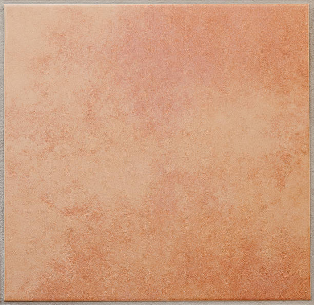 Single apricot colored ceramic tile textured full frame Cloudy, mottled patterned square floor tile, terracotta, surrounded by a grey tile joint or grouting. Red and sandy colored. Italian style. Square orientation. The image has been shot full frame and close up. Ideal for backgrounds. The size of the photo is 2000 x 1943 px. ceramics stock pictures, royalty-free photos & images