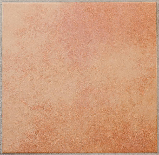 Single apricot colored ceramic tile textured full frame Cloudy, mottled patterned square floor tile, terracotta, surrounded by a grey tile joint or grouting. Red and sandy colored. Italian style. Square orientation. The image has been shot full frame and close up. Ideal for backgrounds. The size of the photo is 2000 x 1943 px. terra cotta tile stock pictures, royalty-free photos & images