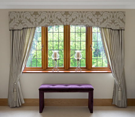 a bedroom window dressed with silk curtains in an expensive luxury new home. The decor has been prepared by a leading Interior Designer. A purple vanity seat balances nicely with the greens of the garden view. A \